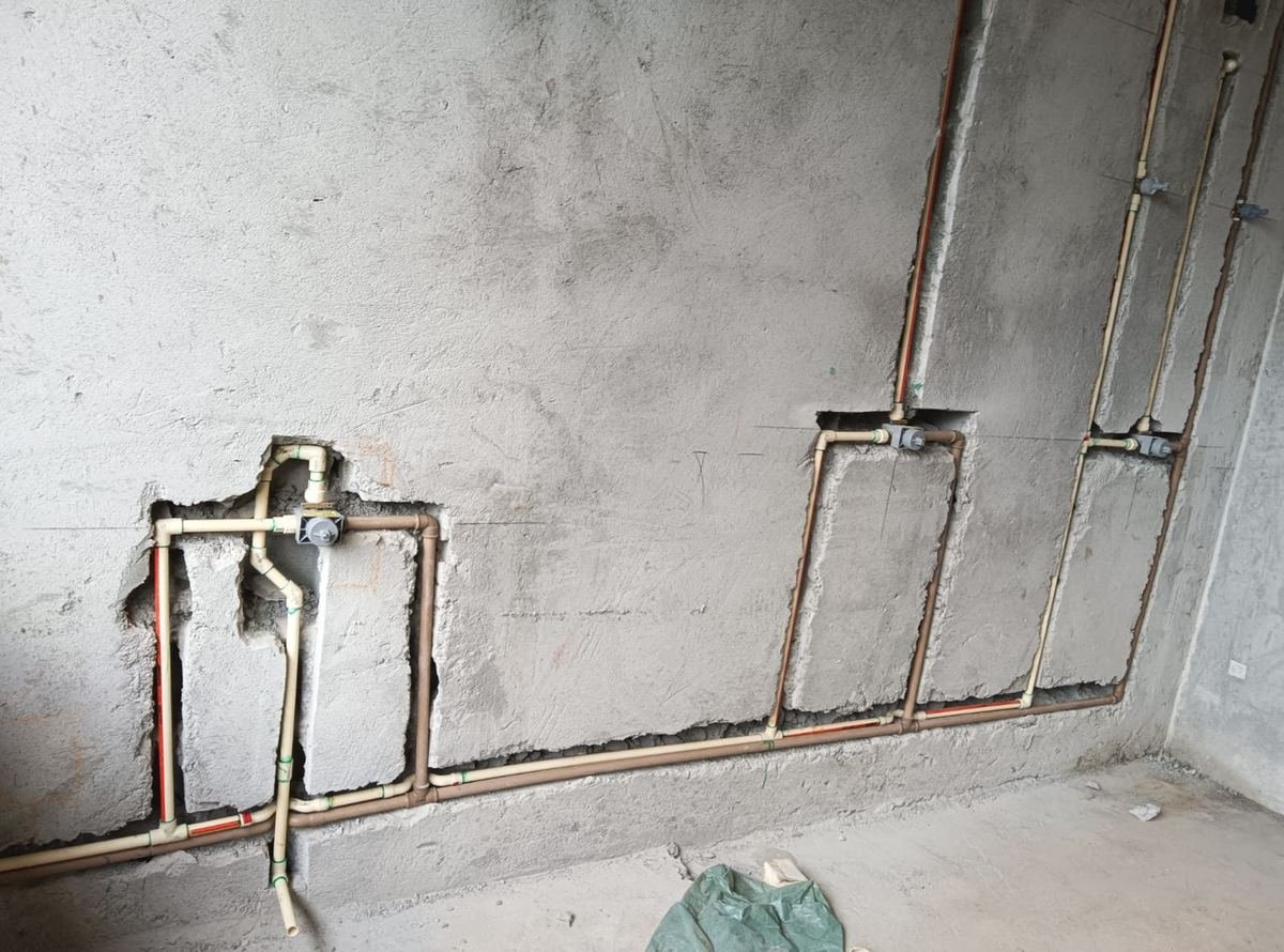 Parede de obra com ramais de tubulação de água embutidos no rasgo, registros instalados e argamassa de fechamento, executados pela J&C Elétrica.