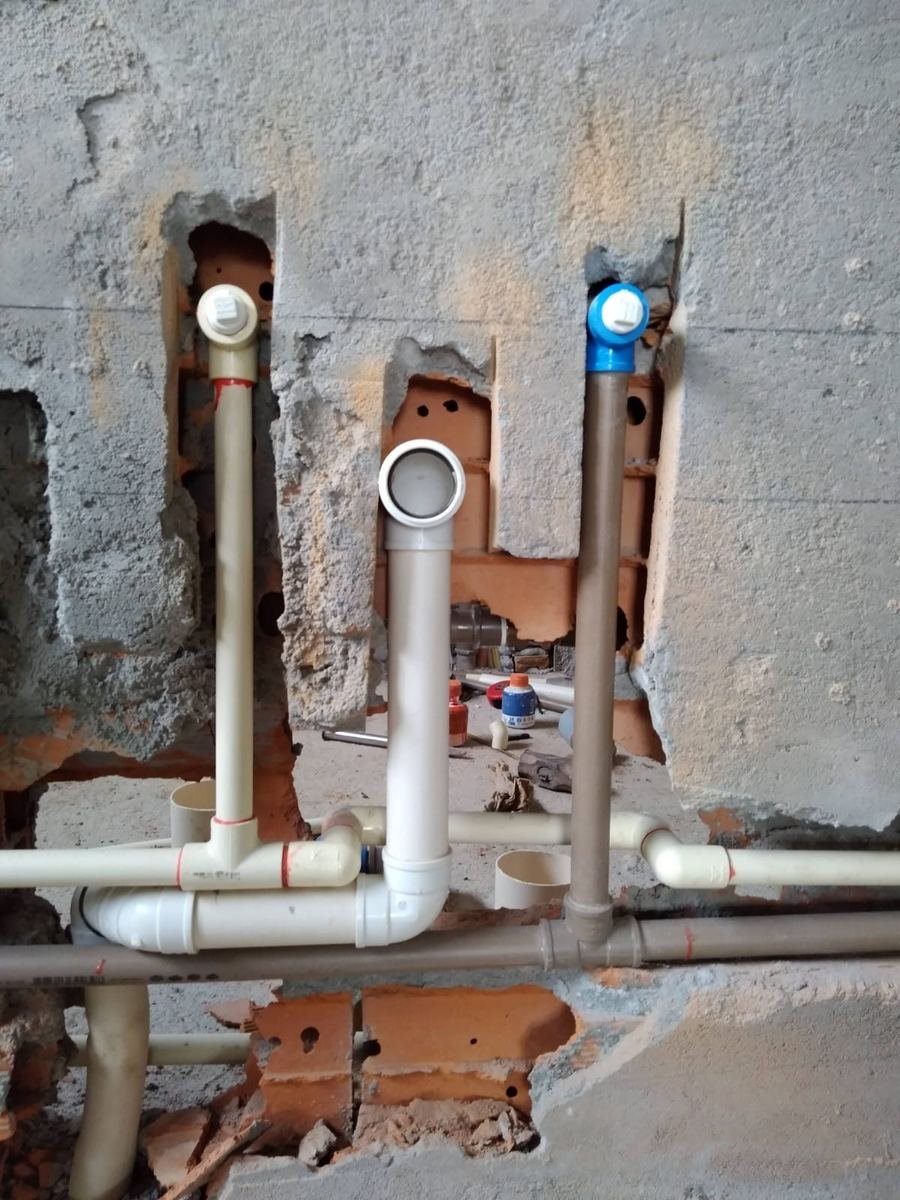 Parede de alvenaria aberta com três tubulações subindo lado a lado, de água quente, esgoto e água fria, com as pontas tampadas, instaladas pela J&C Elétrica.