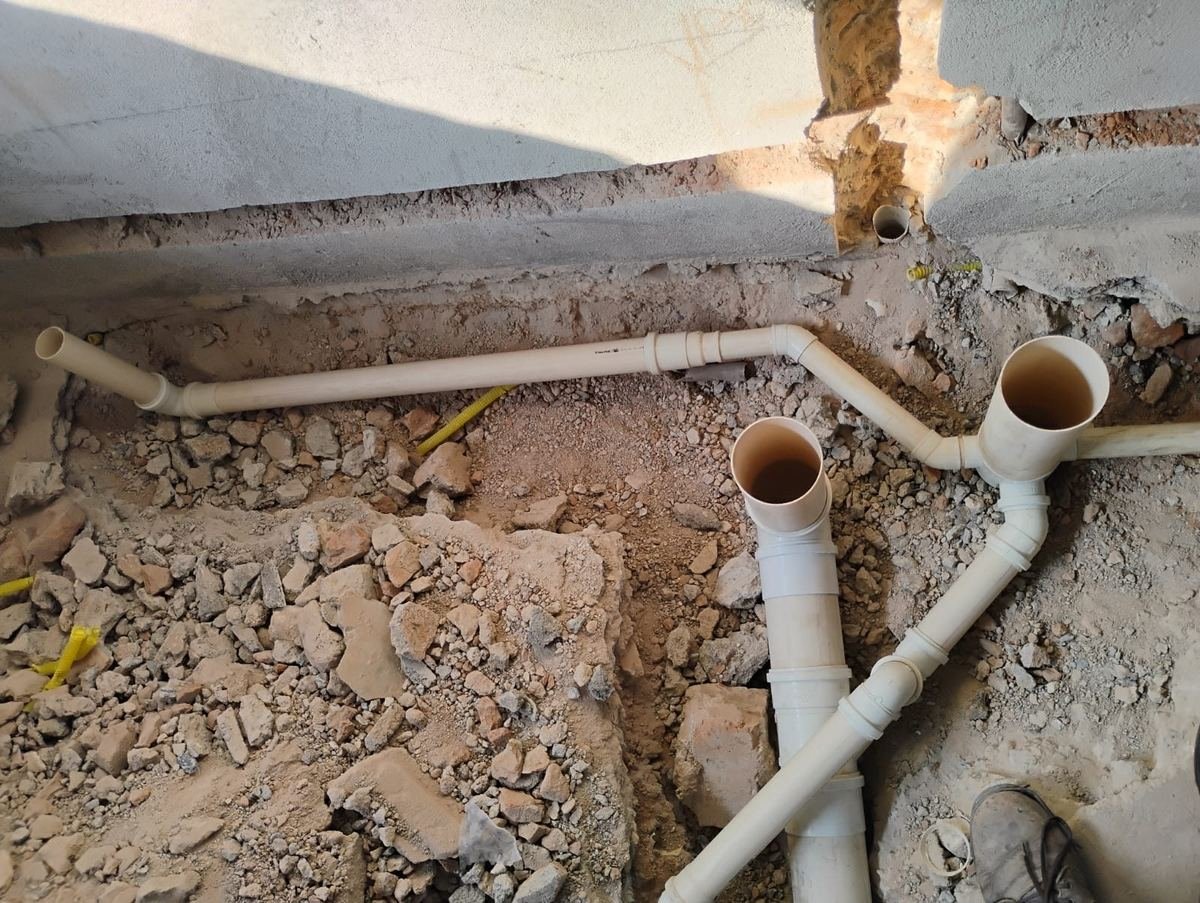 Tubulação de esgoto em PVC branco assentada em vala aberta no solo, com junções e bocas de ligação, executada pela J&C Elétrica.
