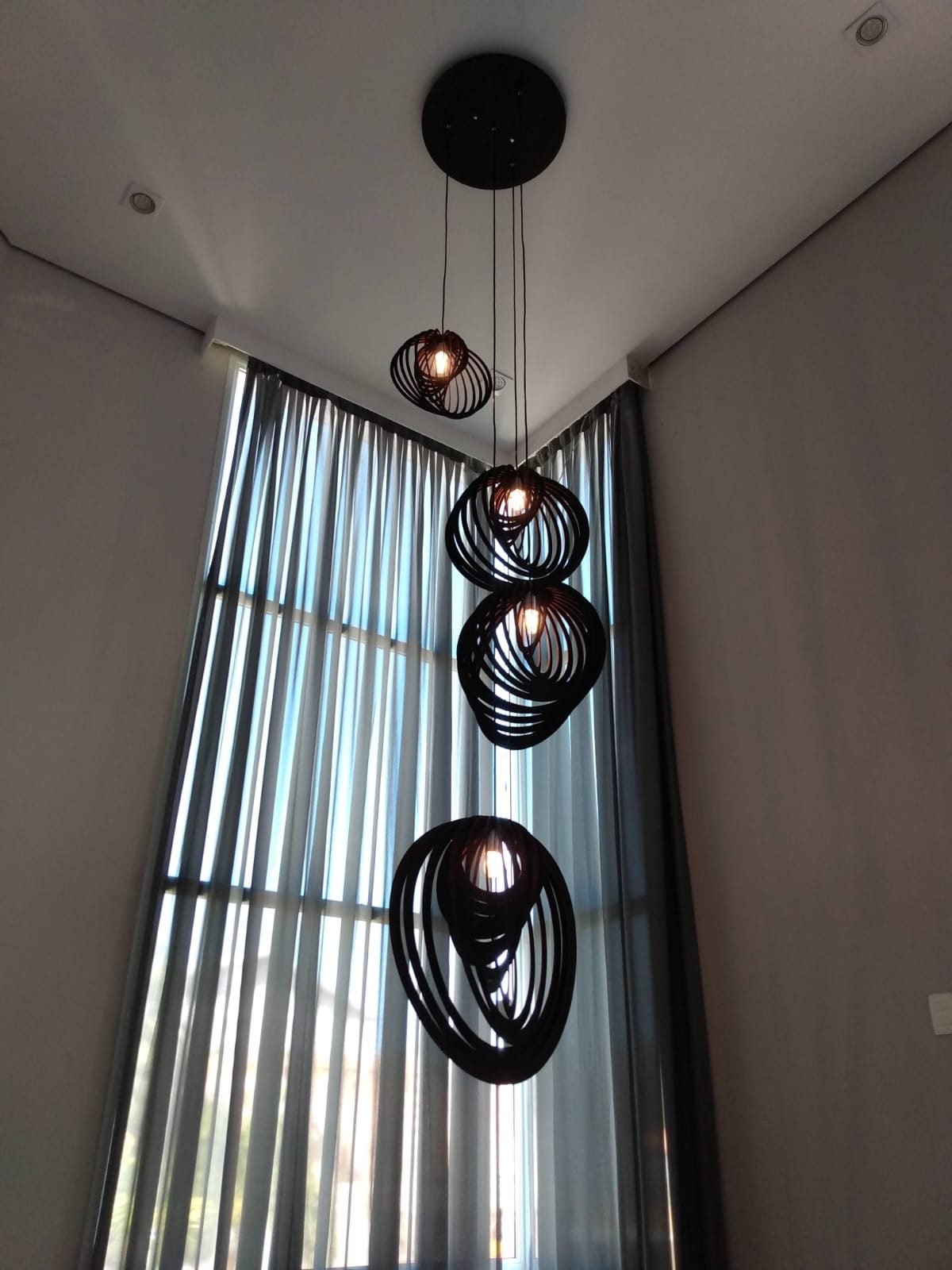 Pendentes suspensos em pé-direito duplo, acesos, diante de uma cortina alta, com a iluminação já entregue e ligada pela J&C Elétrica.