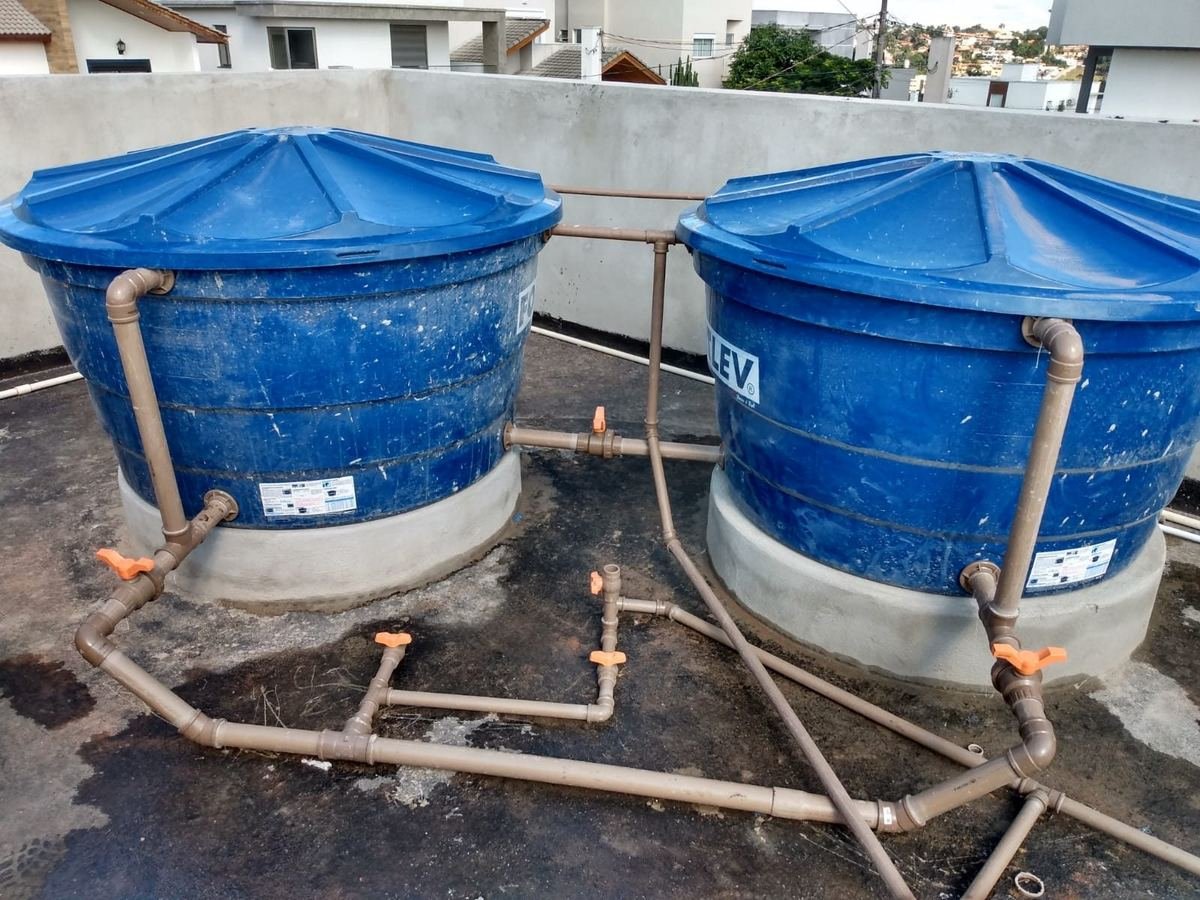Dois reservatórios de água azuis sobre bases de concreto, interligados por barrilete de tubulação com registros de manobra, instalados pela J&C Elétrica.